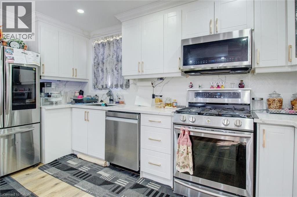 Kitchen with stainless steel appliances, decorative backsplash, light wood-type flooring, white cabinets, and ornamental molding - 823 Queensdale Avenue E, Hamilton, ON - Indoor Photo Showing Kitchen With Upgraded Kitchen