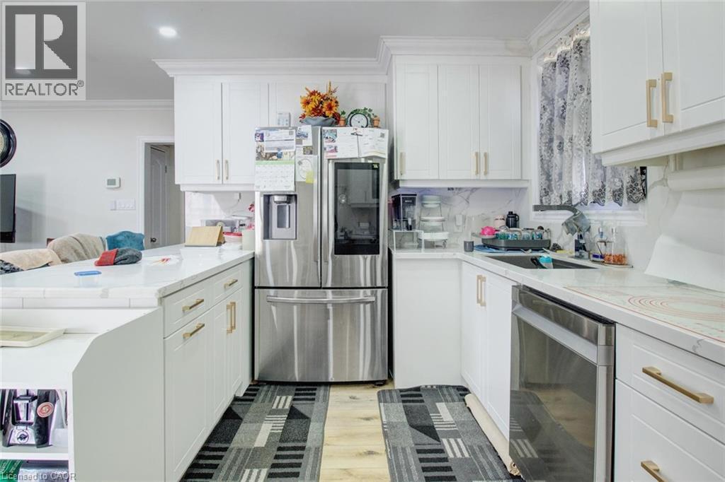 Kitchen featuring stainless steel appliances, ornamental molding, white cabinets, a peninsula, and light wood-type flooring - 823 Queensdale Avenue E, Hamilton, ON - Indoor Photo Showing Kitchen
