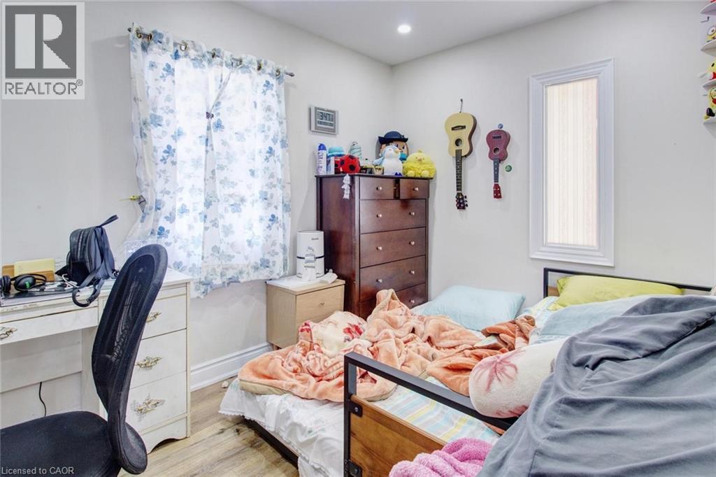 Bright interior space featuring light-colored walls, wood-finish flooring, a rectangular window with white trim, and a second narrow vertical window - 823 Queensdale Avenue E, Hamilton, ON - Indoor Photo Showing Bedroom