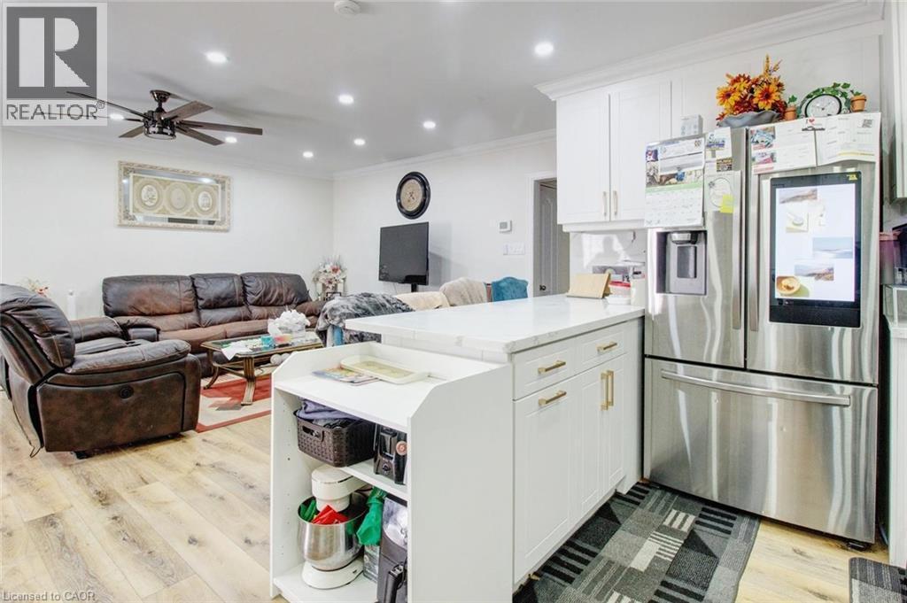 Kitchen with stainless steel fridge with ice dispenser, ornamental molding, a peninsula, light wood finished floors, and open floor plan - 823 Queensdale Avenue E, Hamilton, ON - Indoor