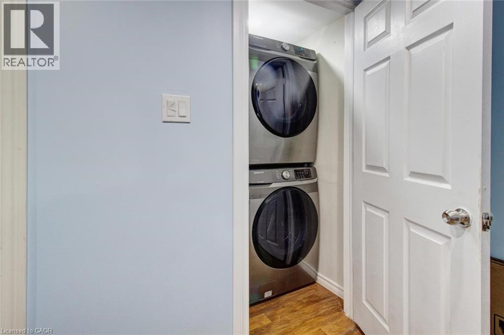 Dedicated laundry area featuring stacked front-load machines, wood-finish flooring, and a paneled interior door - 823 Queensdale Avenue E, Hamilton, ON - Indoor Photo Showing Laundry Room