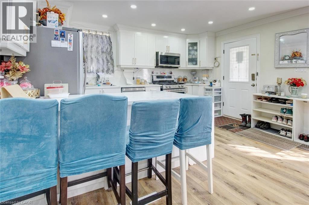 Kitchen with white cabinets, a breakfast bar area, stainless steel appliances, light wood-type flooring, and crown molding - 823 Queensdale Avenue E, Hamilton, ON - Indoor