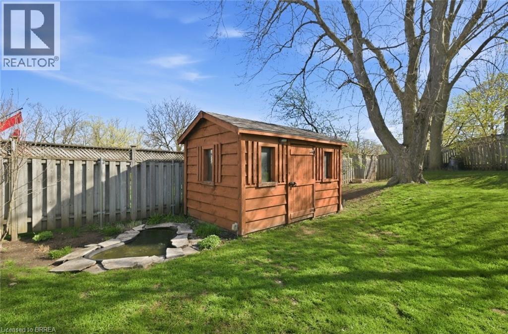 Expansive grassy backyard featuring a wooden shed, a stone-edged pond, a tall privacy fence, and mature trees - 71 Pinecrest Drive, Kitchener, ON - Outdoor