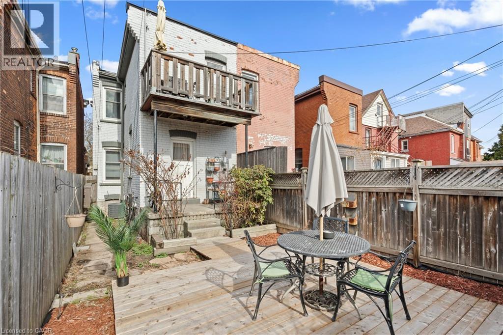 Rear exterior featuring a ground-level wood deck, a second-story balcony with wood railings, a white painted brick facade, and a private wooden fence - 78 Clyde Street, Hamilton, ON - Outdoor With Deck Patio Veranda