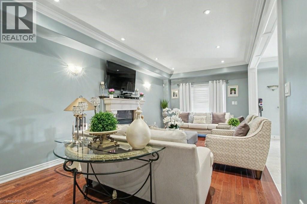 Living room featuring crown molding, a raised ceiling, a glass covered fireplace, dark wood-style flooring, and recessed lighting - 284 Normanhurst Avenue, Hamilton, ON - Indoor