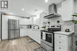Kitchen featuring stainless steel appliances, range hood, white cabinetry, light wood-style floors, and light stone countertops -
