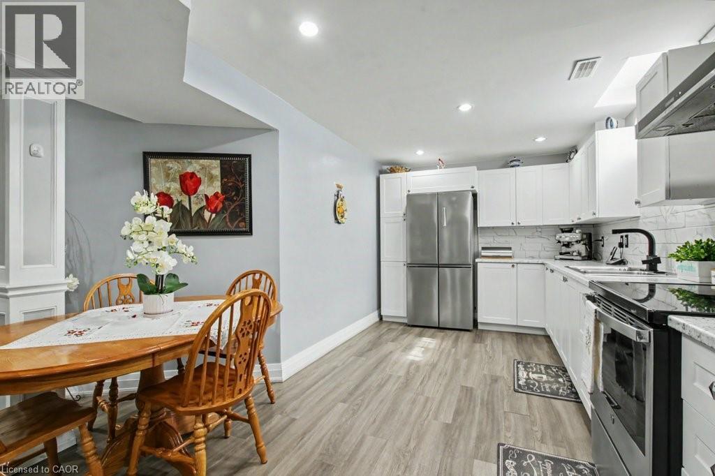 Kitchen with stainless steel appliances, white cabinets, light wood-style floors, range hood, and light stone counters - 284 Normanhurst Avenue, Hamilton, ON - Indoor