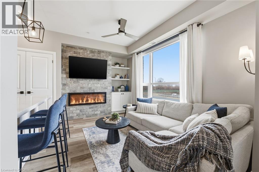 Living area featuring a ceiling fan, built in features, light wood-style flooring, and a stone fireplace - 120 Springvalley Crescent Unit# 203, Hamilton, ON - Indoor Photo Showing Living Room With Fireplace