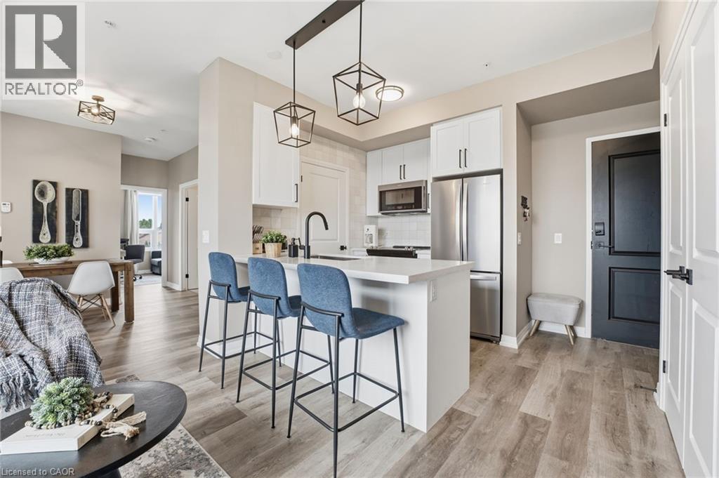 Kitchen featuring white cabinets, a kitchen bar, stainless steel appliances, a peninsula, and light wood-style floors - 120 Springvalley Crescent Unit# 203, Hamilton, ON - Indoor Photo Showing Kitchen With Stainless Steel Kitchen With Upgraded Kitchen