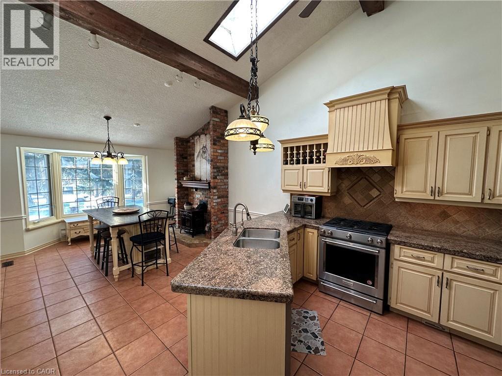 Kitchen featuring cream cabinets, stainless steel gas range oven, a peninsula, and light tile patterned flooring - 5590 Blind Line, Burlington, ON - Indoor Photo Showing Kitchen With Double Sink