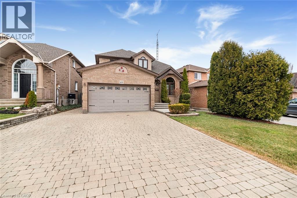 View of front of property with an attached garage, decorative driveway, brick siding, and a front lawn - 40 Artistic Boulevard, Hamilton, ON - Outdoor With Facade