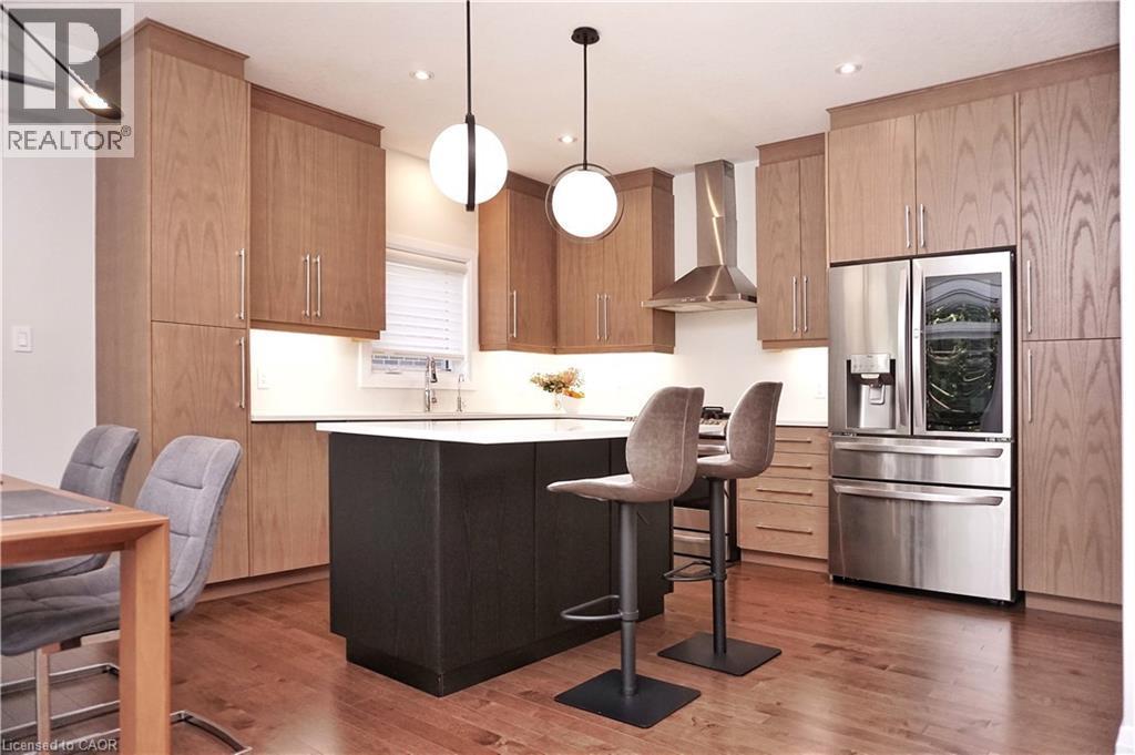 Kitchen featuring stainless steel fridge with ice dispenser, a kitchen breakfast bar, a kitchen island, dark wood-type flooring, and decorative light fixtures - 63 Ian Ormston Drive, Kitchener, ON - Indoor