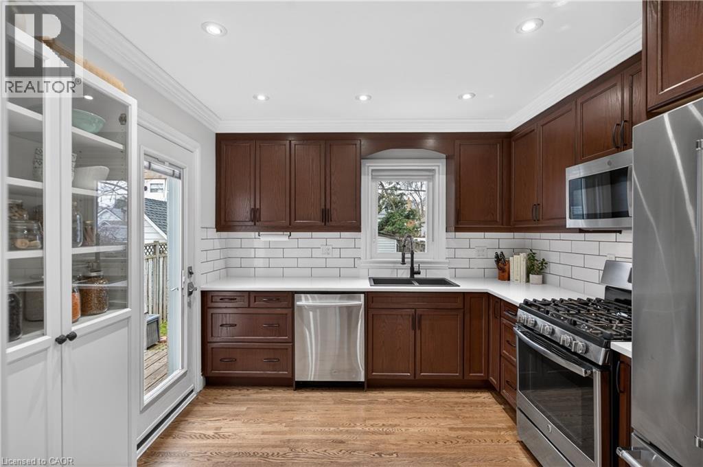 Kitchen with stainless steel appliances, crown molding, light wood-style flooring, dark wood finish cabinets, and tasteful backsplash - 248 London Street S, Hamilton, ON - Indoor Photo Showing Kitchen With Double Sink