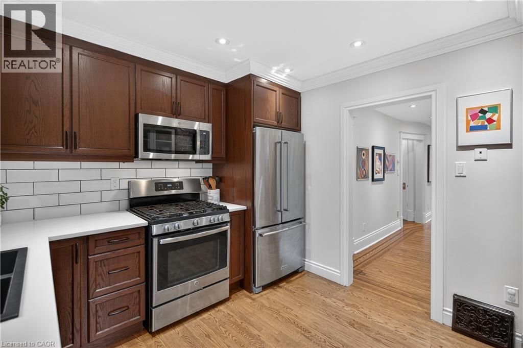 Kitchen with stainless steel appliances, tasteful backsplash, dark wood finish cabinetry, light wood-style flooring, and recessed lighting - 248 London Street S, Hamilton, ON - Indoor Photo Showing Kitchen