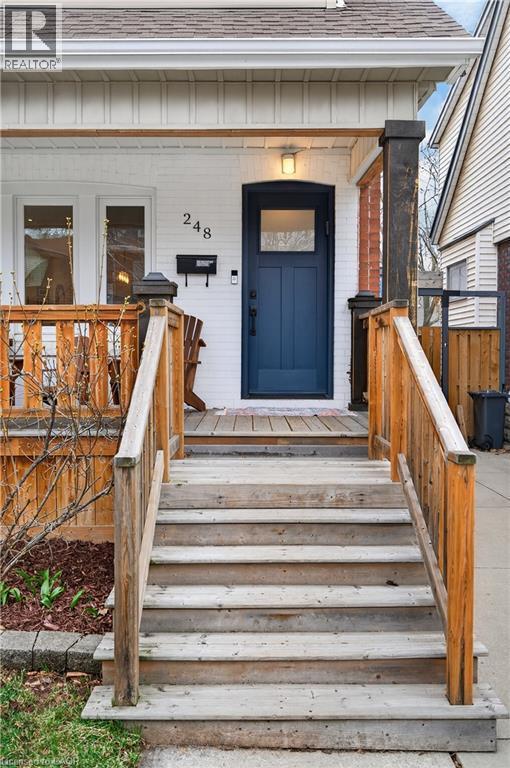 Property entrance with roof with shingles, brick siding, a wooden deck, and board and batten siding - 248 London Street S, Hamilton, ON - Outdoor With Exterior