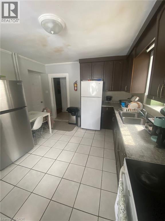 Kitchen with white appliances, dark wood finish cabinets, light tile patterned floors, light countertops, and ornamental molding - 9 Waterloo Avenue, Guelph, ON - Indoor Photo Showing Kitchen With Double Sink