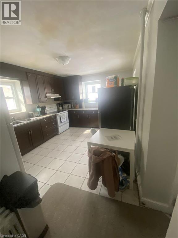 Kitchen with dark wood finish cabinets, freestanding refrigerator, light tile patterned floors, electric stove, and light countertops - 9 Waterloo Avenue, Guelph, ON - Indoor