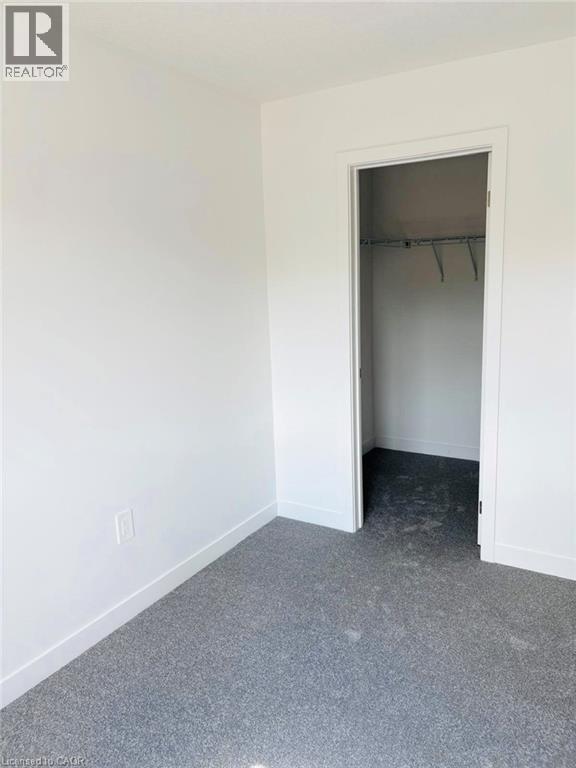Unfurnished bedroom with a spacious closet and dark colored carpet - 7 Pin Oak Common, Cambridge, ON - Indoor Photo Showing Other Room