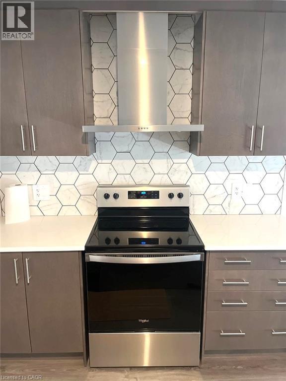 Kitchen featuring wall chimney range hood, stainless steel electric stove, and modern cabinets - 7 Pin Oak Common, Cambridge, ON - Indoor Photo Showing Kitchen