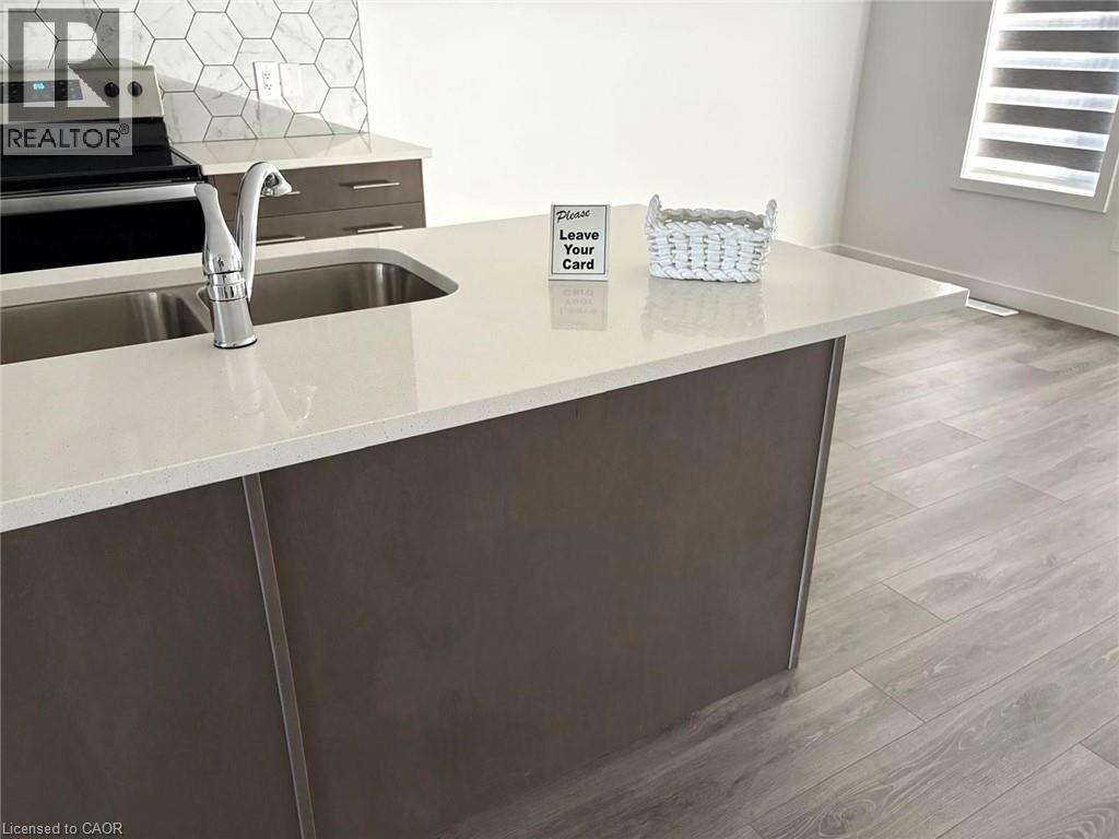 Kitchen with dark brown cabinetry, stainless steel range with electric cooktop, light stone counters, and light wood-style floors - 7 Pin Oak Common, Cambridge, ON - Indoor Photo Showing Kitchen With Double Sink