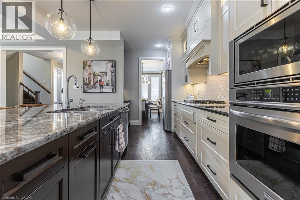 Dual tone kitchen with stainless steel appliances, dual tone cabinetry, hanging light fixtures, dark stone counters, and dark wood-type flooring - 2719 Torrey Pines Way, London, ON - Indoor Photo Showing Kitchen With Upgraded Kitchen
