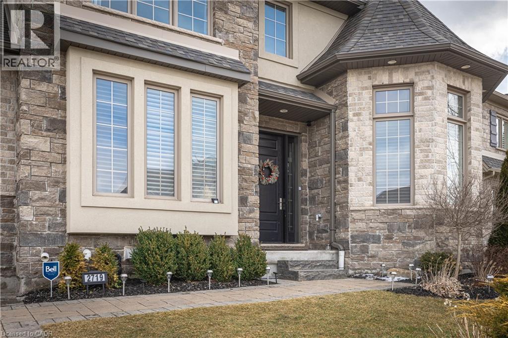 Entrance to property featuring stone siding, stucco siding, a yard, and a shingled roof - 2719 Torrey Pines Way, London, ON - Outdoor