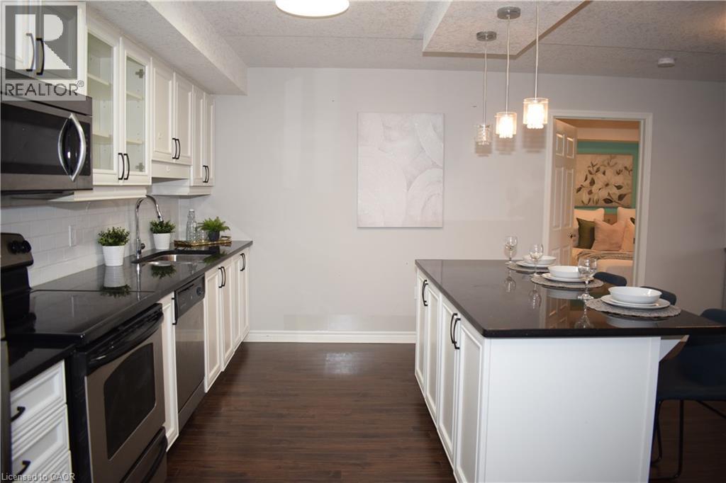 Kitchen with white cabinets, stainless steel appliances, dark stone counters, a breakfast bar area, and glass insert cabinets - 776 Laurelwood Drive Unit# 406, Waterloo, ON - Indoor Photo Showing Kitchen With Upgraded Kitchen