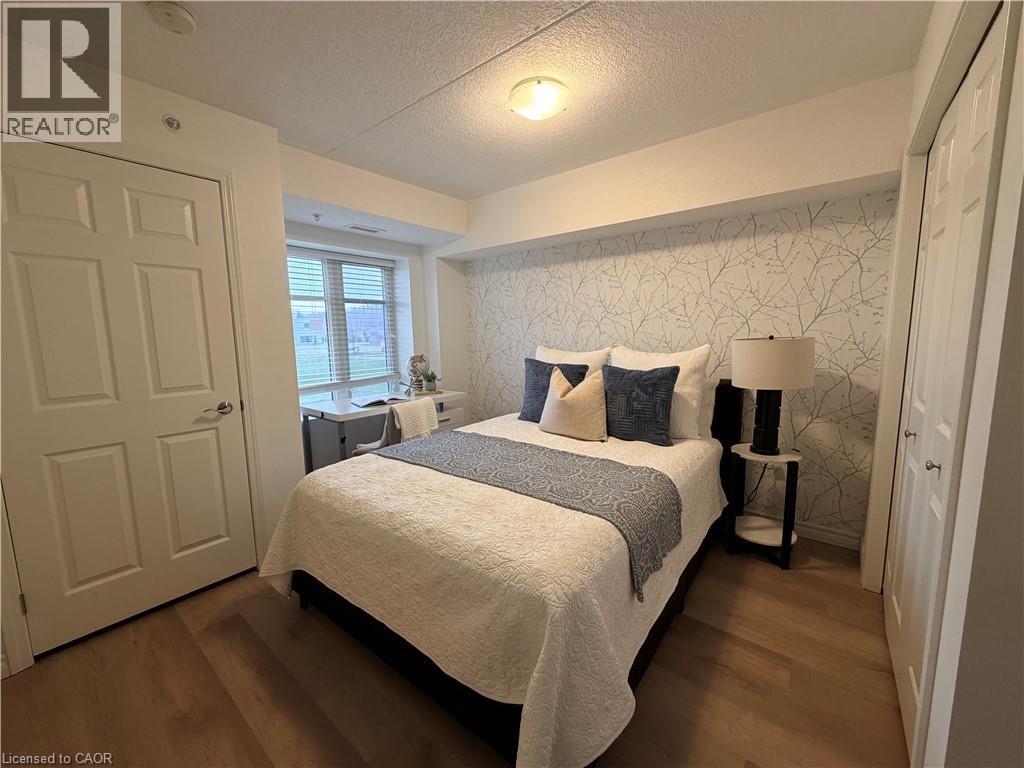 Bedroom with a closet, a textured ceiling, dark wood finished floors, wallpapered walls, and an accent wall - 776 Laurelwood Drive Unit# 406, Waterloo, ON - Indoor Photo Showing Bedroom