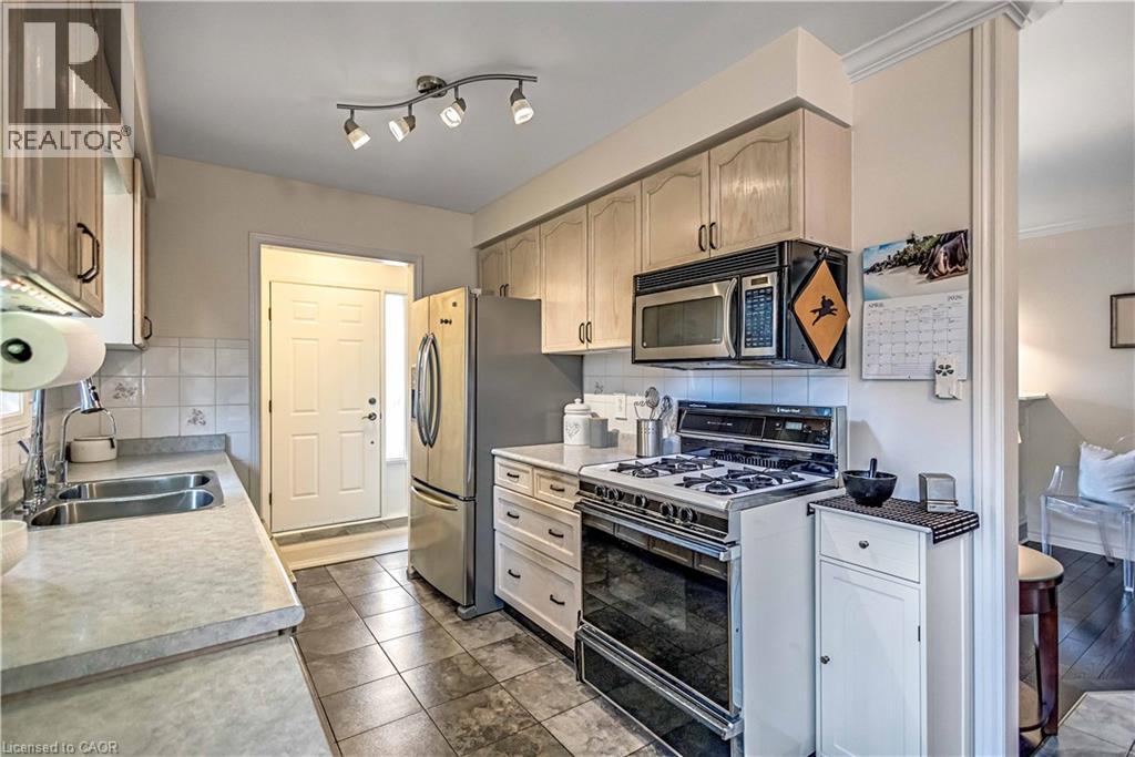 Kitchen featuring stainless steel appliances, light countertops, backsplash, and dark tile patterned floors - 640 Acadia Drive, Hamilton, ON - Indoor Photo Showing Kitchen With Double Sink