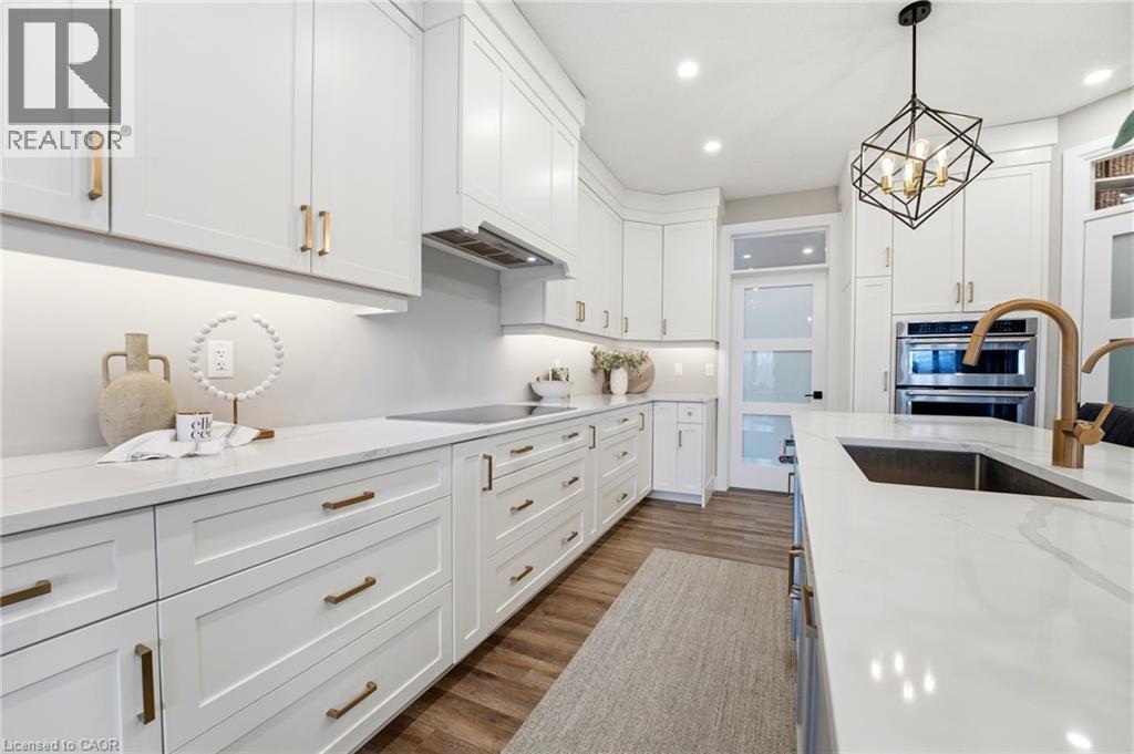 Kitchen featuring white cabinetry, light stone countertops, stainless steel double oven, dark wood-type flooring, and suspended lighting - 39 Mill Race Crescent, St. Jacobs, ON - Indoor Photo Showing Kitchen With Upgraded Kitchen