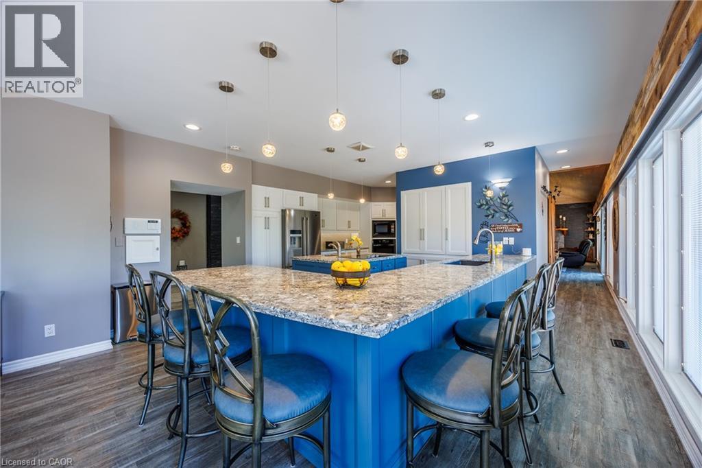 Kitchen featuring hanging light fixtures, high end fridge, light stone countertops, a breakfast bar, and dark wood finished floors - 1285 Cockshutt Road, Simcoe, ON - Indoor