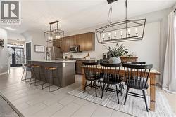 Kitchen with suspended lighting, a kitchen bar, a center island with sink, stainless steel appliances, and light tile patterned floors -