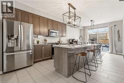 Kitchen with stainless steel appliances, an island with sink, a breakfast bar, suspended lighting, and light stone counters -