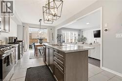 Kitchen featuring open floor plan, hanging lights, dark wood finish cabinetry, a center island with sink, and light tile patterned floors -