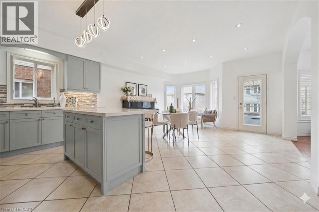 Open-concept kitchen and dining area featuring light-toned cabinetry, a central island with countertop seating, tiled flooring, and multiple windows - 512 Wood Nettle Way, Waterloo, ON - Indoor Photo Showing Kitchen