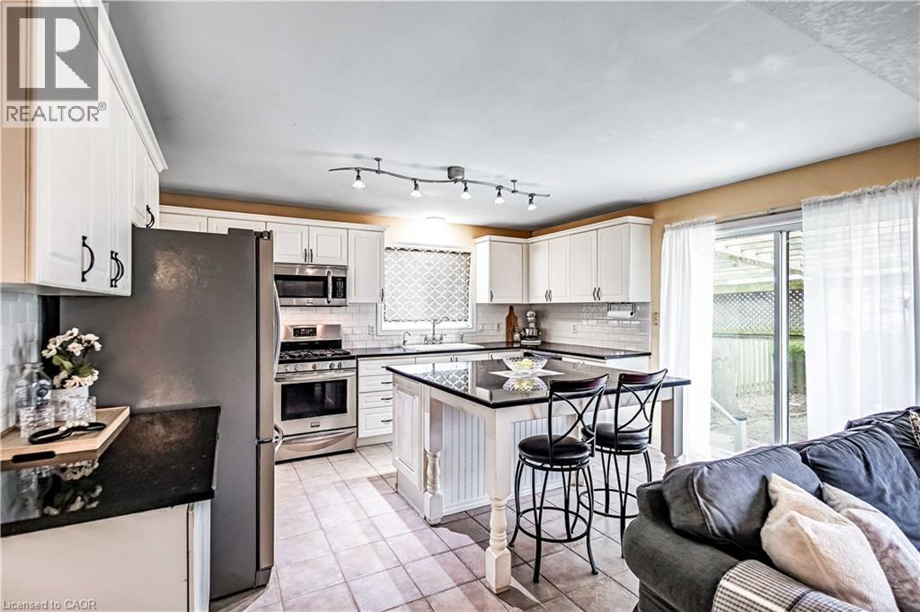 Kitchen featuring stainless steel appliances, white cabinets, light tile patterned flooring, and a breakfast bar area - 65 Thistlemoor Drive, Caledonia, ON - Indoor Photo Showing Kitchen
