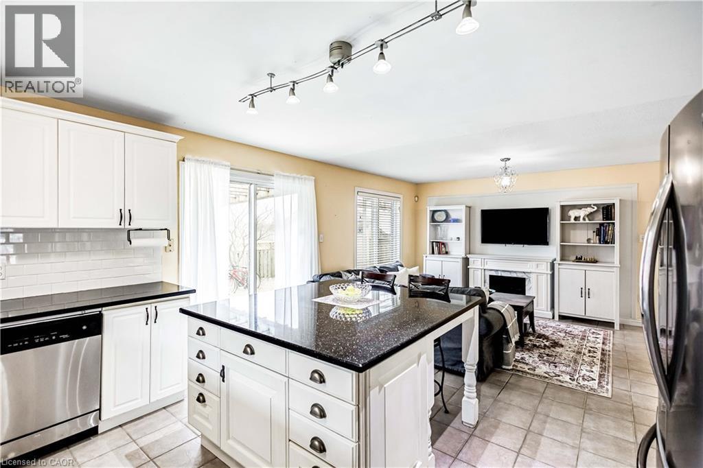 Kitchen featuring stainless steel appliances, open floor plan, light tile patterned floors, white cabinetry, and dark stone counters - 65 Thistlemoor Drive, Caledonia, ON - Indoor Photo Showing Kitchen