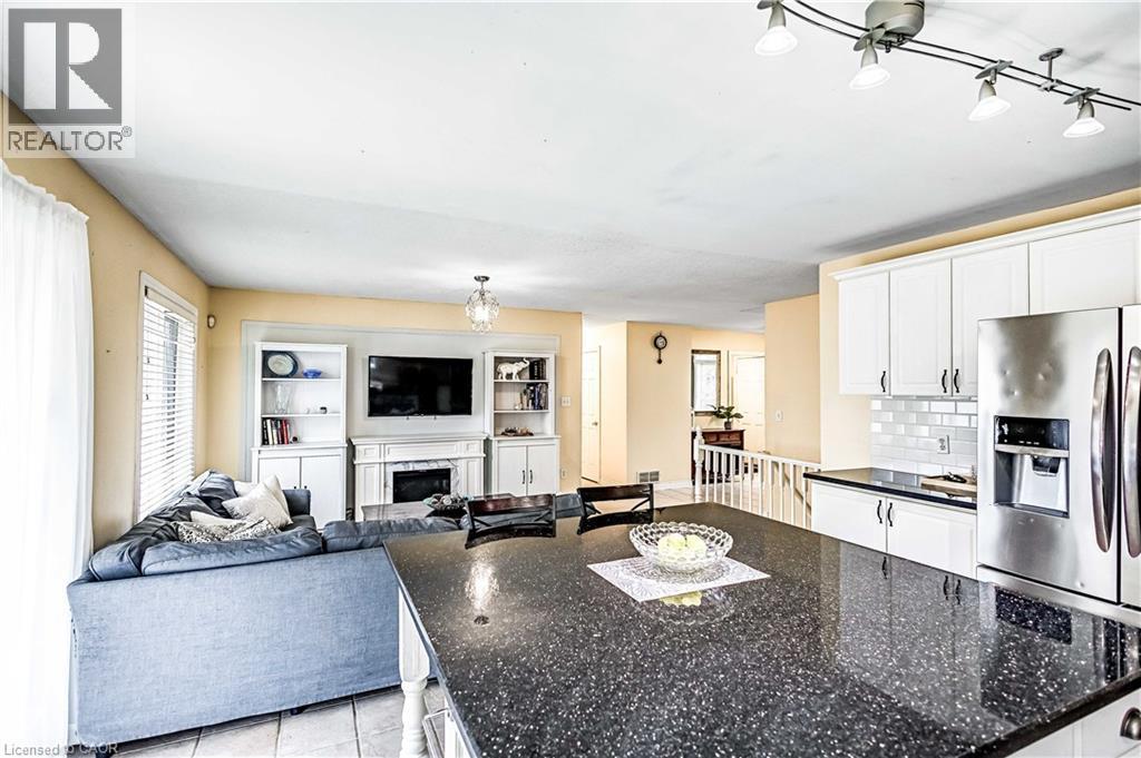 Kitchen featuring white cabinets, a chandelier, a high end fireplace, dark stone countertops, and light tile patterned floors - 65 Thistlemoor Drive, Caledonia, ON - Indoor With Fireplace