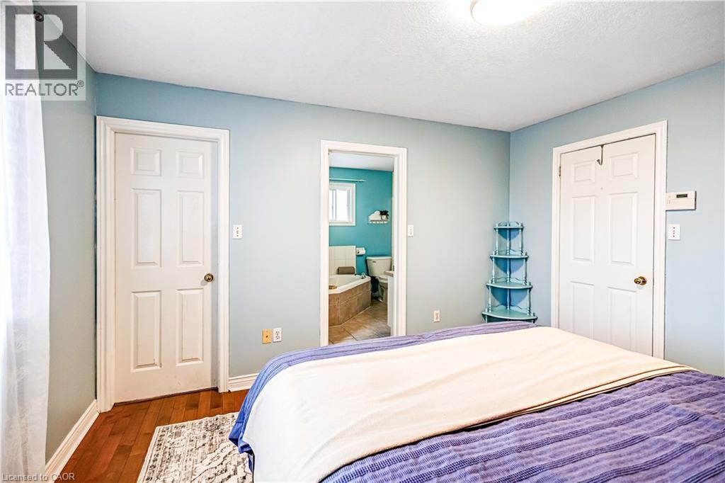Bedroom with dark wood-style flooring, connected bathroom, and a textured ceiling - 65 Thistlemoor Drive, Caledonia, ON - Indoor Photo Showing Bedroom