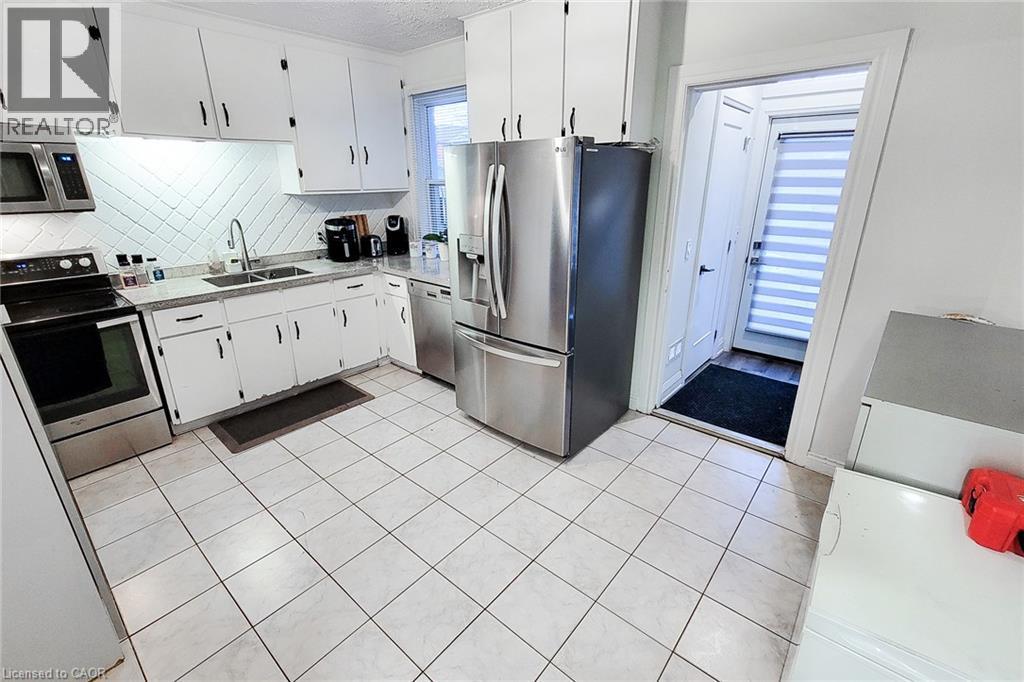 Kitchen featuring stainless steel appliances, white cabinets, light tile patterned flooring, and tasteful backsplash - 97 Keith Street, Hamilton, ON - Indoor Photo Showing Kitchen With Stainless Steel Kitchen With Double Sink