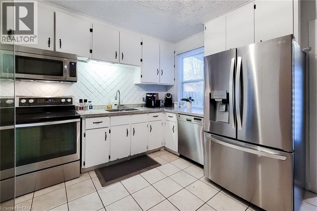 Kitchen with stainless steel appliances, white cabinetry, a textured ceiling, backsplash, and light tile patterned floors - 97 Keith Street, Hamilton, ON - Indoor Photo Showing Kitchen With Stainless Steel Kitchen With Double Sink
