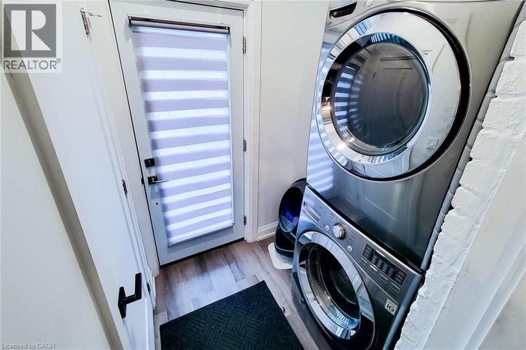 Laundry area with wood finished floors and stacked washing machine and dryer - 97 Keith Street, Hamilton, ON - Indoor Photo Showing Laundry Room