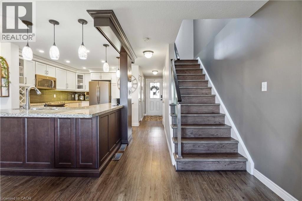 Dual tone kitchen with light stone counters, glass fronted cabinets, stainless steel appliances, dark wood-style floors, and hanging light fixtures - 27 Red Clover Crescent, Kitchener, ON - Indoor Photo Showing Kitchen