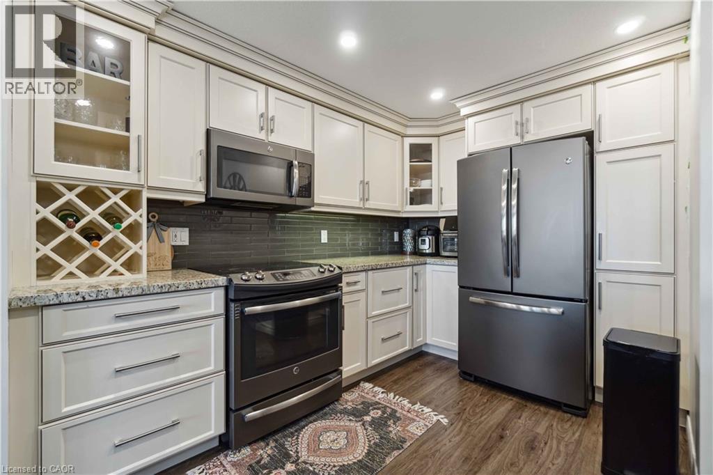Kitchen with glass fronted cabinets, stainless steel appliances, white cabinetry, dark wood-type flooring, and light stone countertops - 27 Red Clover Crescent, Kitchener, ON - Indoor Photo Showing Kitchen With Stainless Steel Kitchen