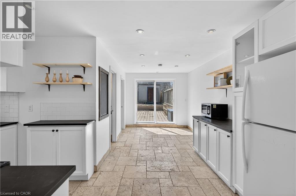 Kitchen featuring open shelves, dark countertops, freestanding refrigerator, stone tile flooring, and white cabinets - 216 Robert Street, Hamilton, ON - Indoor Photo Showing Kitchen
