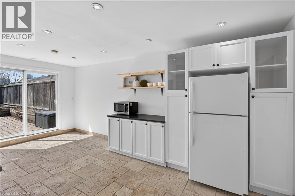 Kitchen featuring freestanding refrigerator, open shelves, white cabinetry, stone tile floors, and dark countertops - 216 Robert Street, Hamilton, ON - Indoor