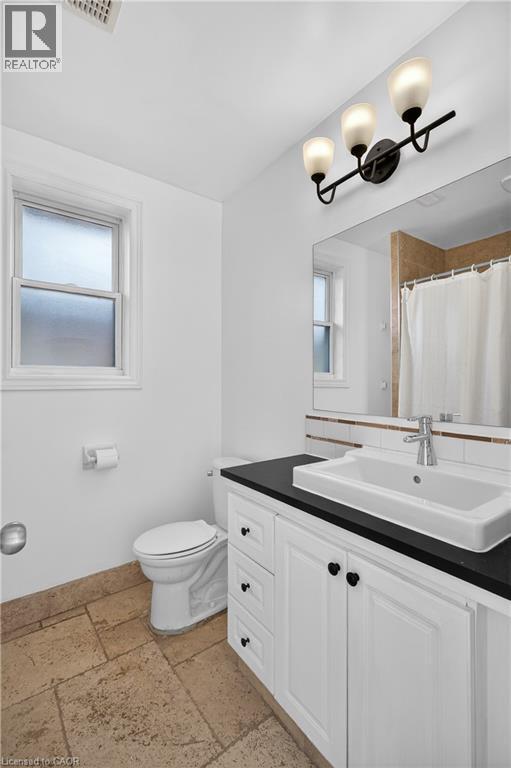 Full bath with stone tile flooring, vanity, curtained shower, and plenty of natural light - 216 Robert Street, Hamilton, ON - Indoor Photo Showing Bathroom