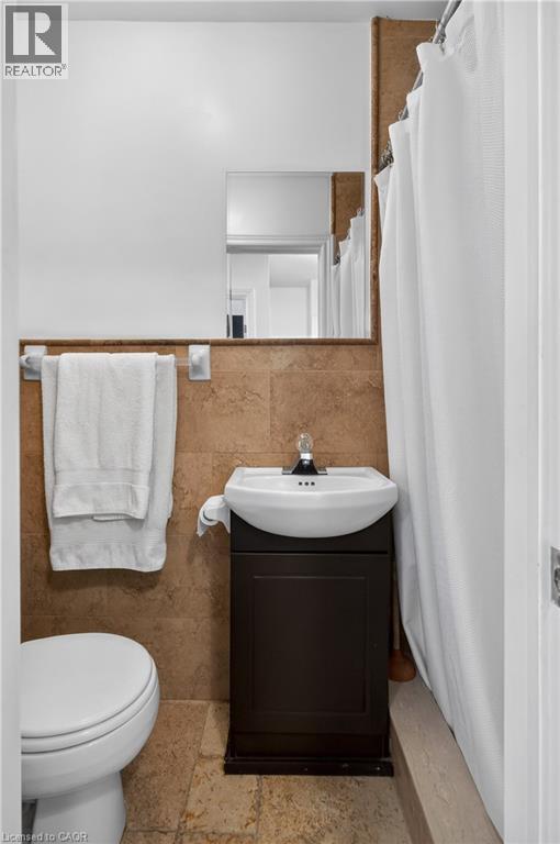 Full bathroom featuring a shower with curtain, vanity, tile walls, stone tile flooring, and wainscoting - 216 Robert Street, Hamilton, ON - Indoor Photo Showing Bathroom