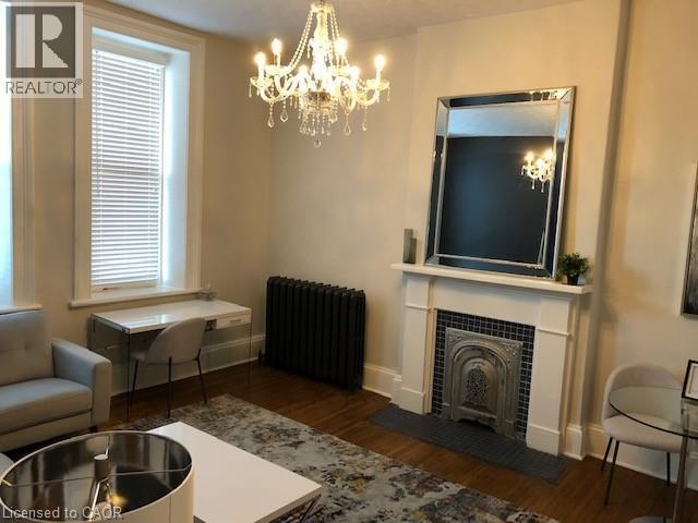 Living room with radiator, dark wood-style flooring, and a chandelier - 14 Duke Street, Hamilton, ON - Indoor Photo Showing Living Room With Fireplace