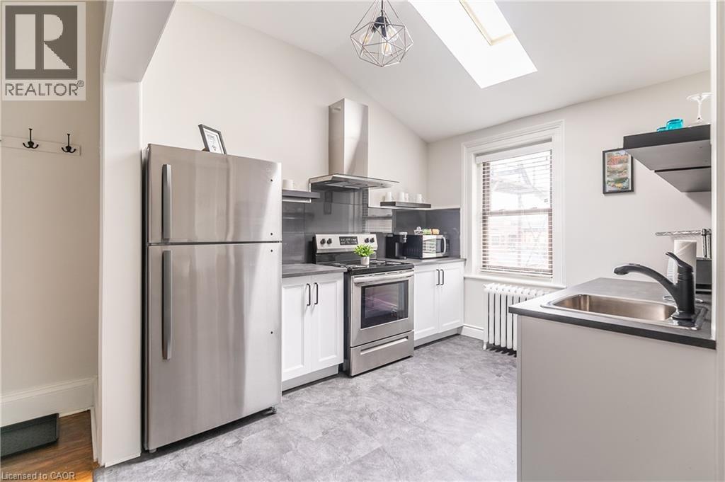 Kitchen with stainless steel appliances, white cabinets, range hood, vaulted ceiling, and a skylight - 14 Duke Street, Hamilton, ON - Indoor Photo Showing Kitchen